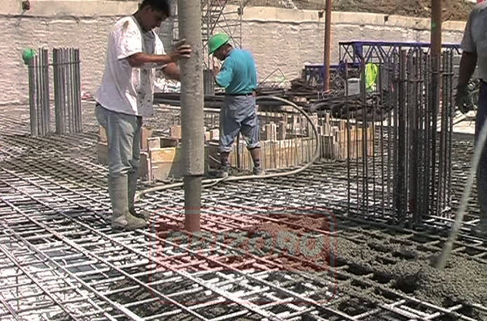 Людина зі шлангом з бетононасосу з якого виходить бетон